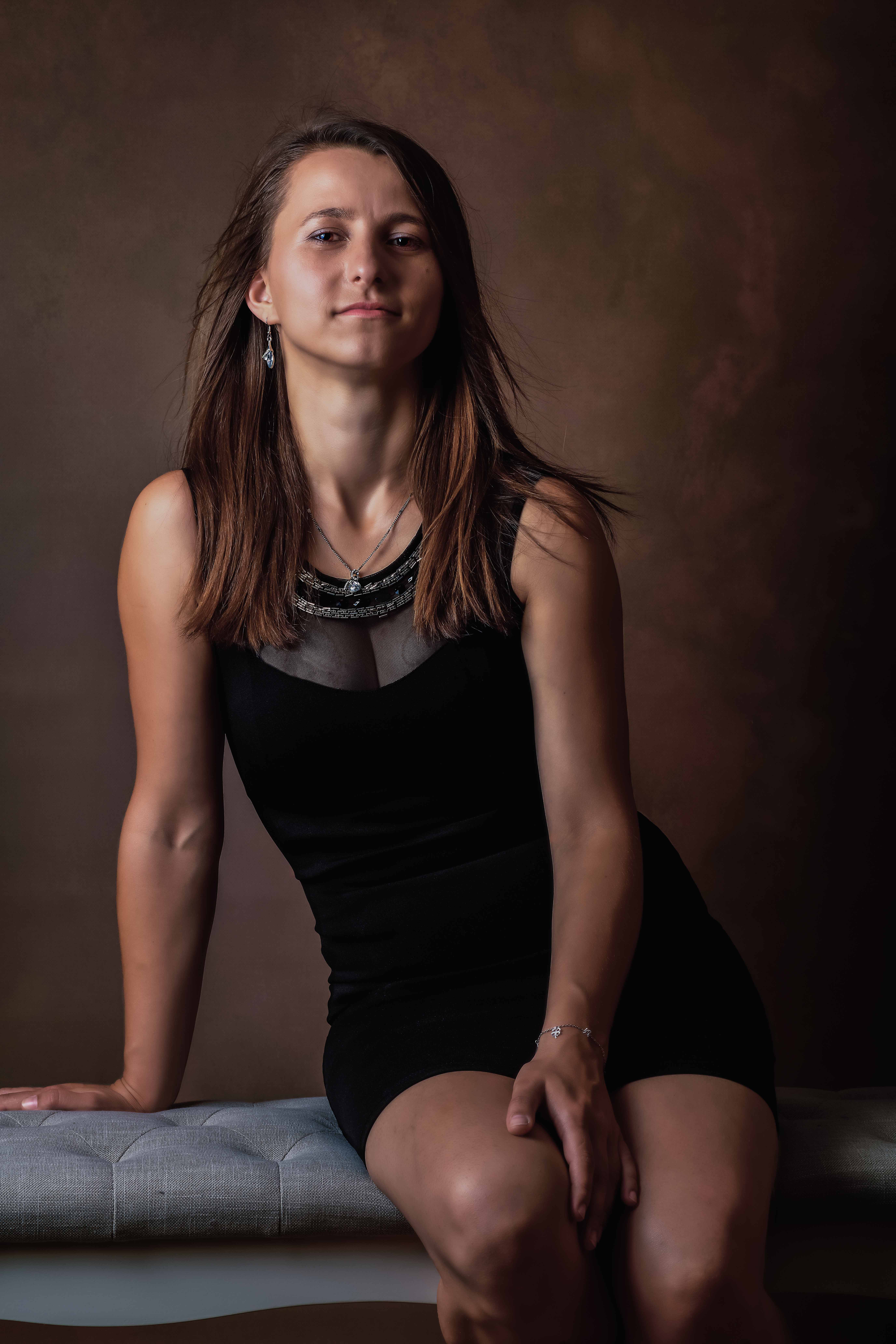 Portret kobiety wykonany w studio na brązowym tle, siedząc na ławeczce.