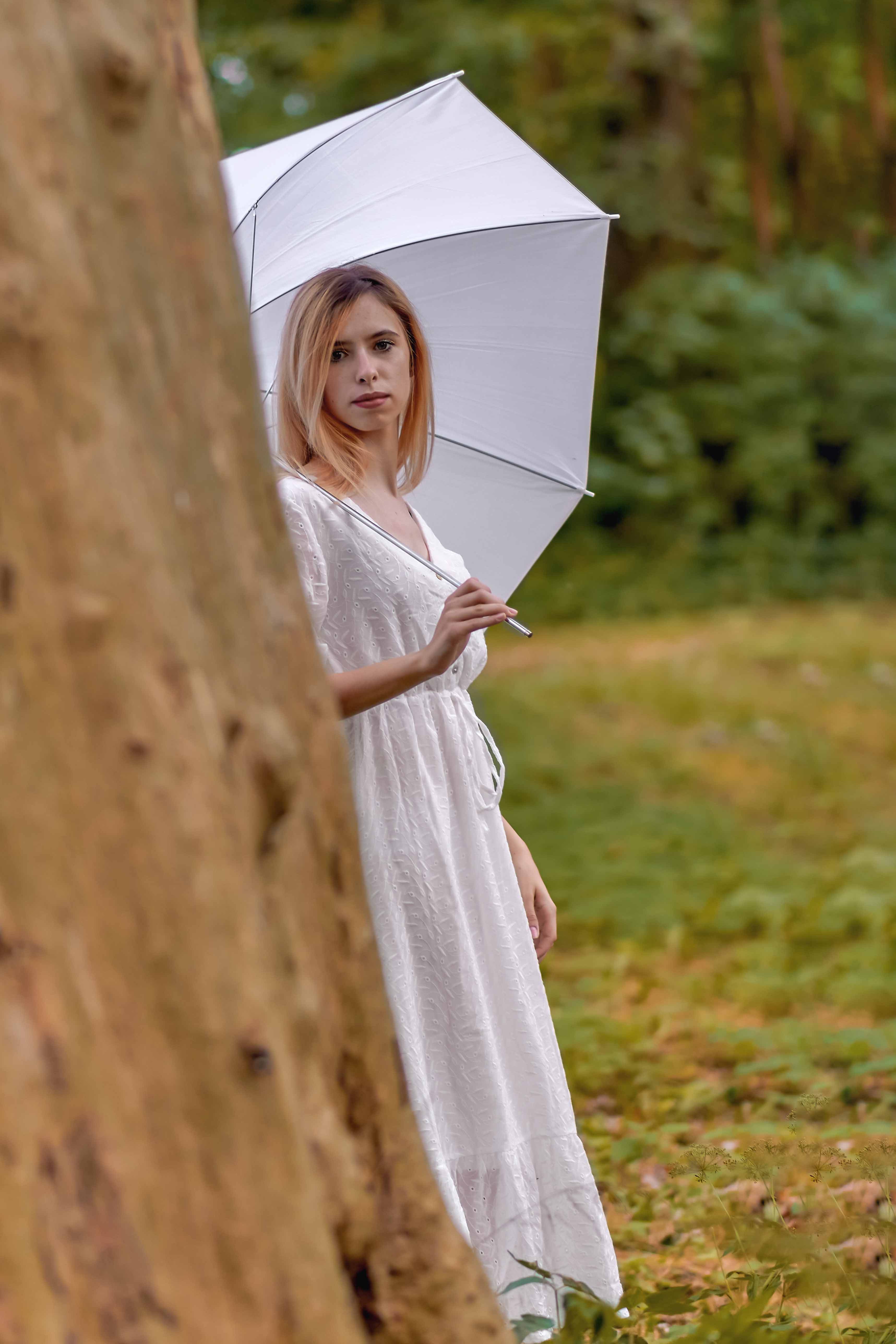 Kobieta w eleganckiej sukni podczas plenerowej sesji portretowej w z białym parasolem.