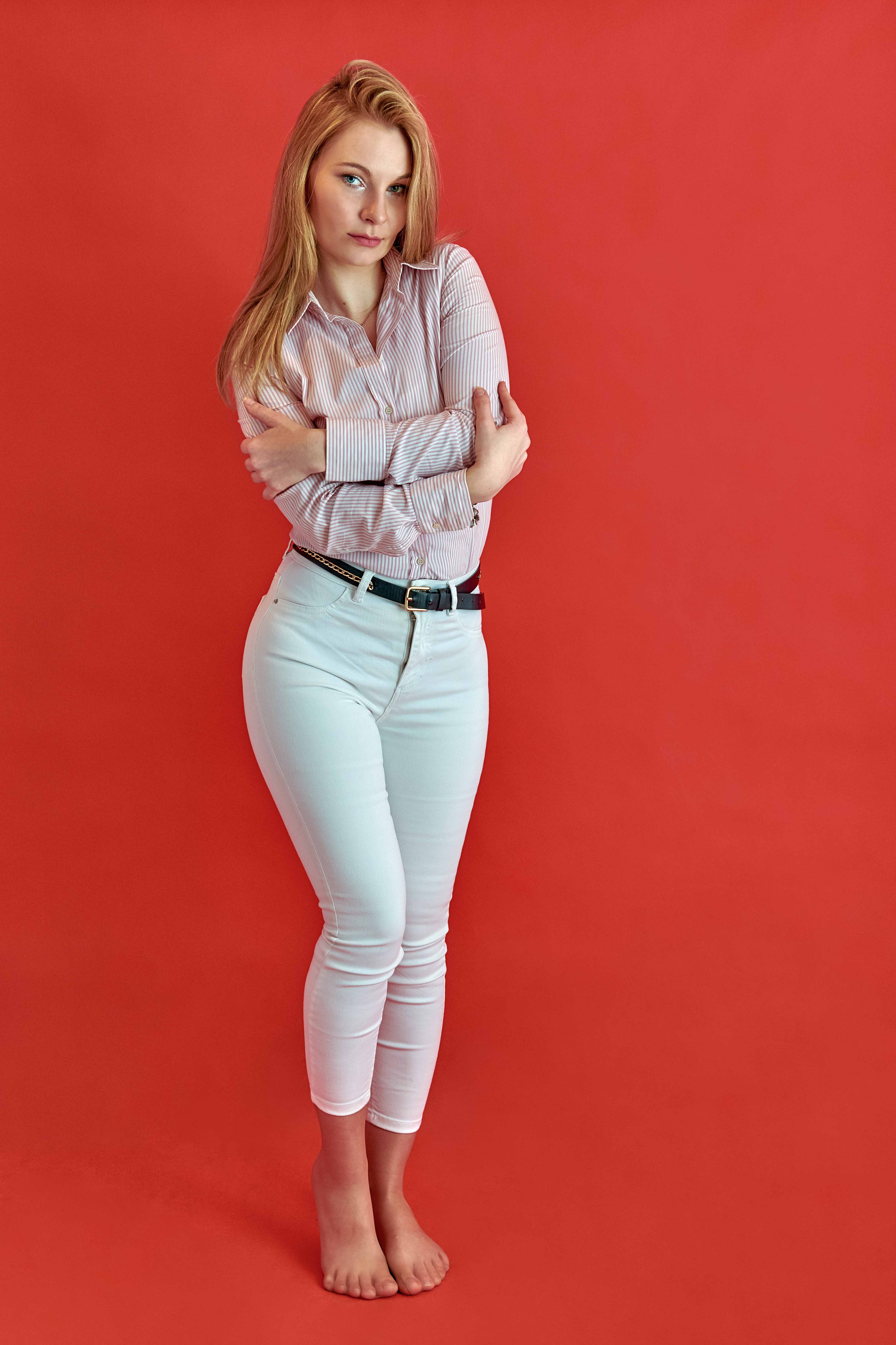 Portret kobiety w eleganckiej stylizacji wykonany w studio na czerwonym tle stojąca na wprost