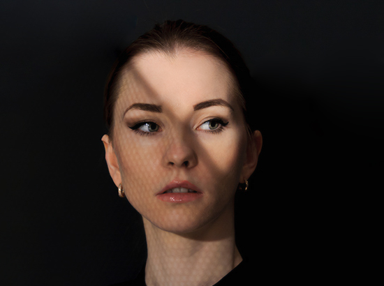 Zmysłowy portret modelki na czarnym tle ze światłem przysłaniającym twarz.